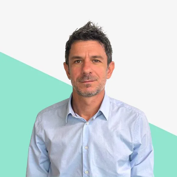 Man in a light blue shirt against a geometric background.