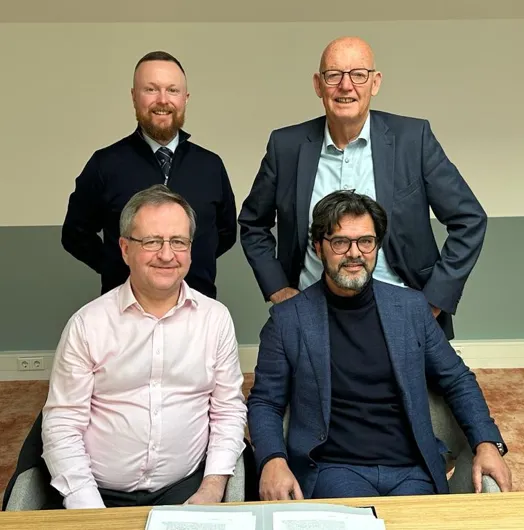 Four men posing for a photo in an office setting.