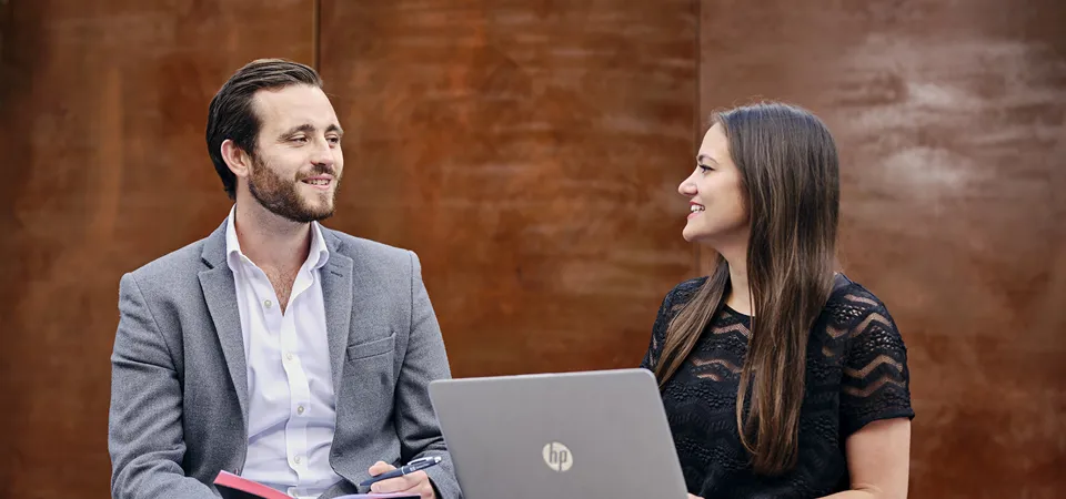 man and woman discussing work with a laptop and notebook