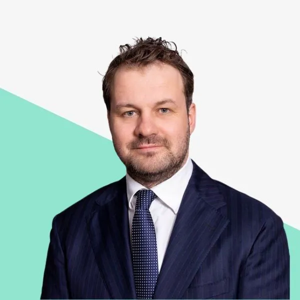 Man in a suit with a tie, against a light background.